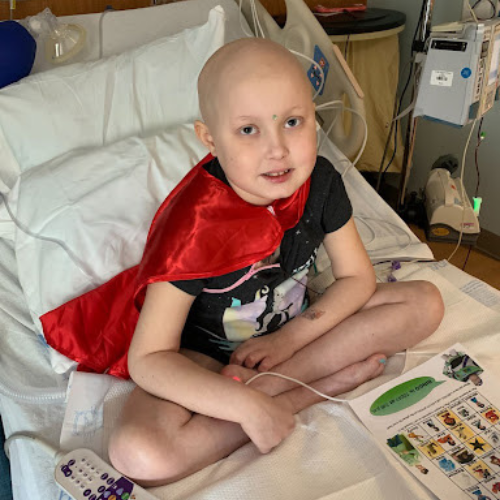 Maura with Acute Lymphoblastic Leukemia cancer sitting on hospital bed. Pediatric oncology, g-tube, losing hair, chemo symptoms, chemo hair loss, childhood cancer, pediatric cancer.