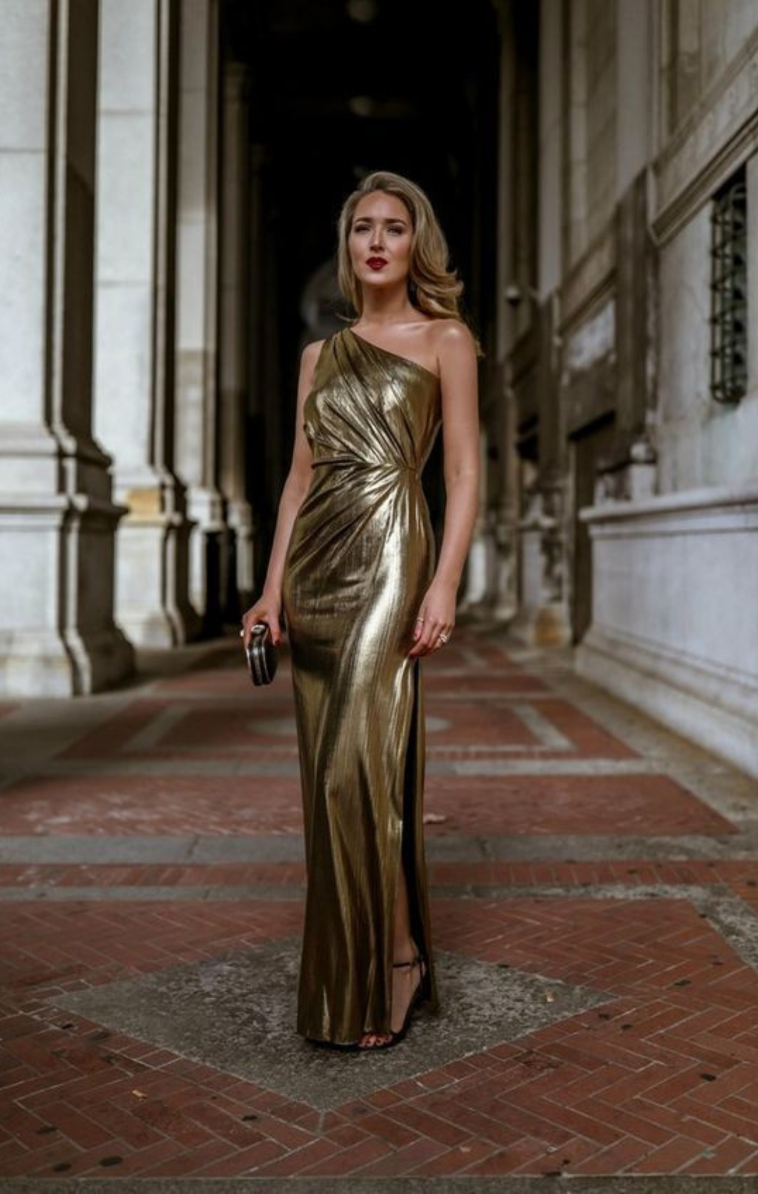 Woman in long gold dress with one sleeve and a clutch.