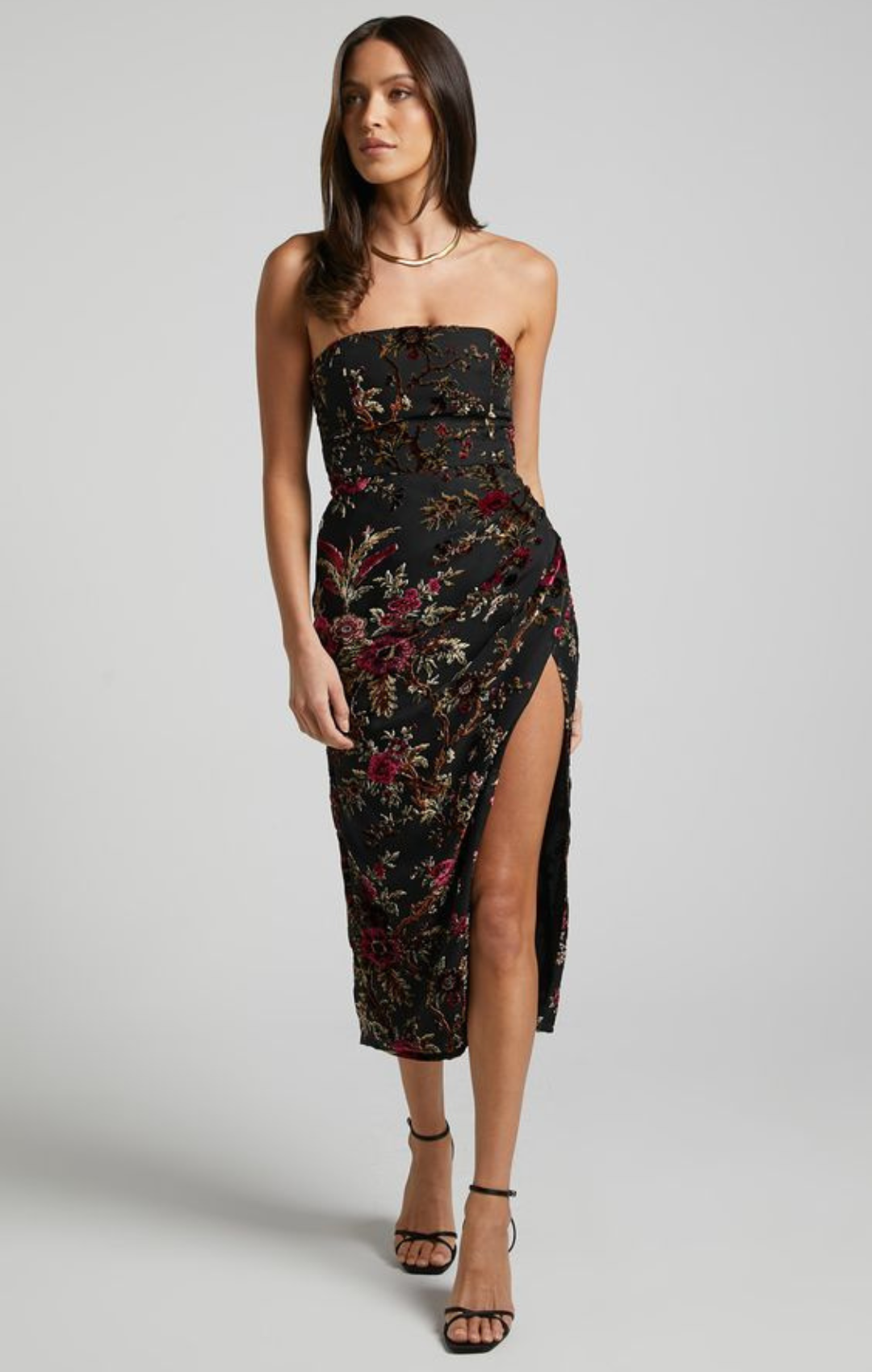 Woman in sleeveless black dress with floral pattern and slit.