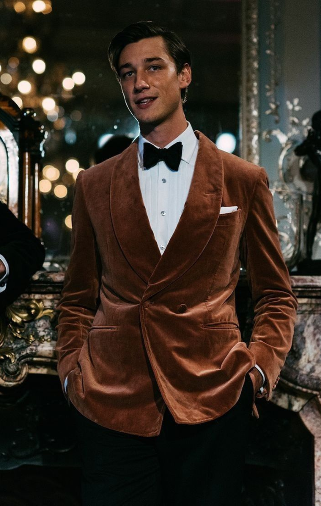 Man in copper colored, velvet suit jacket with black bow tie and white shirt.