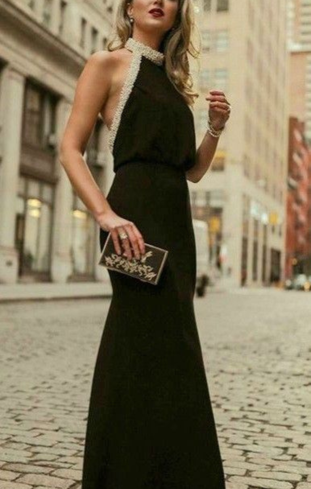 Woman in long, black, halter neck dress with clutch.